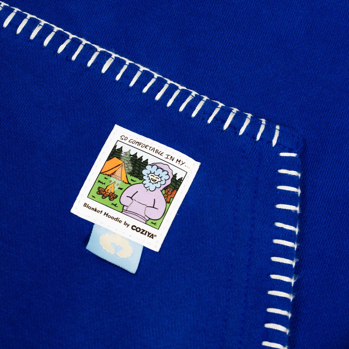 Close-up of the blanket-stitch seam and the Coziya mascot label on the pocket