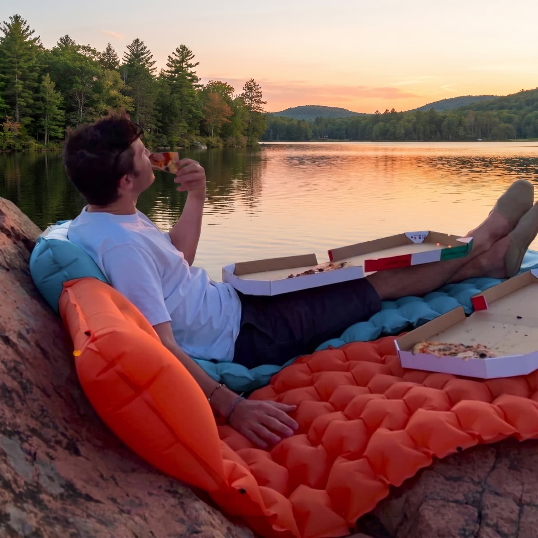 Man relaxing on Coziya inflatable sleeping pad in lounger position by a lake at sunset